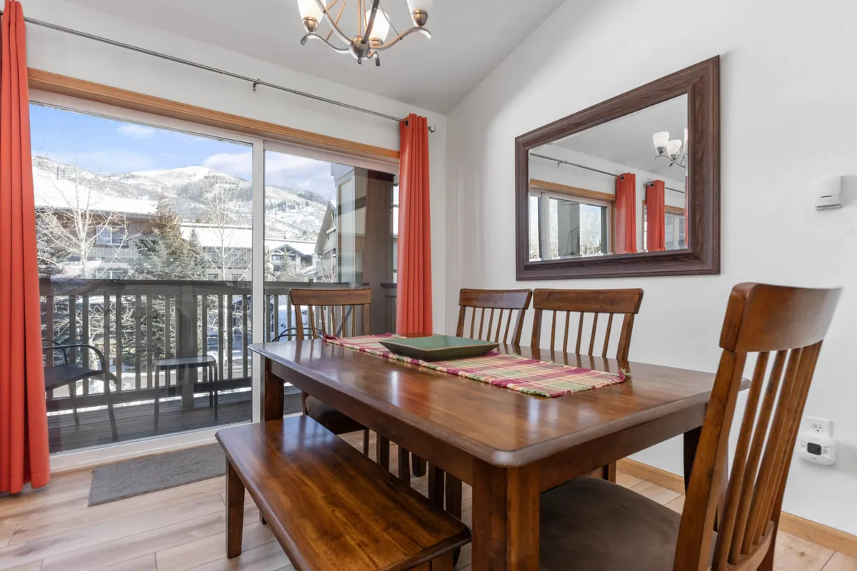 An interior scene showing a dining table situated by a large window with a panoramic mountain view. The cozy space is accented by a decorative mirror, creating a warm and inviting setting ideal for intimate meals, family gatherings, or quiet coffee mornings with a view.