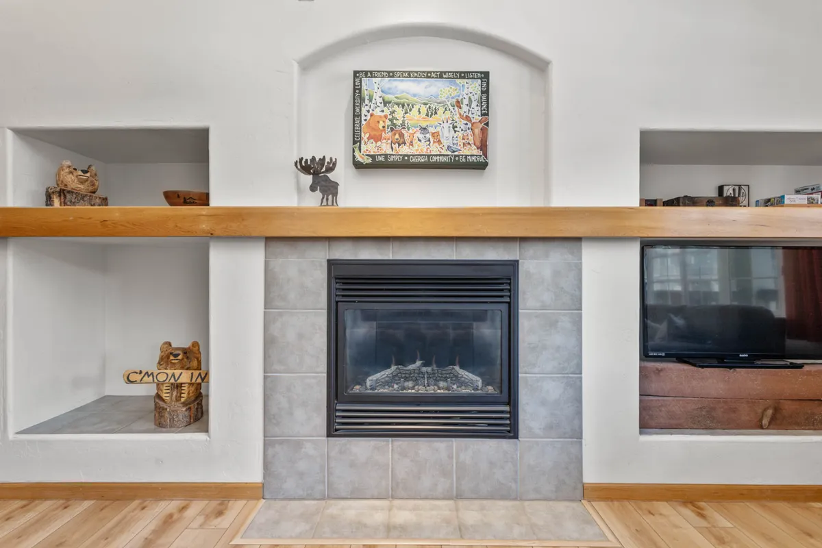 A living room featuring a cozy fireplace, stylish artwork, and a television, offering a welcoming space for relaxation and socializing. The decor and arrangement highlight comfort and the enjoyment of home-like leisure.