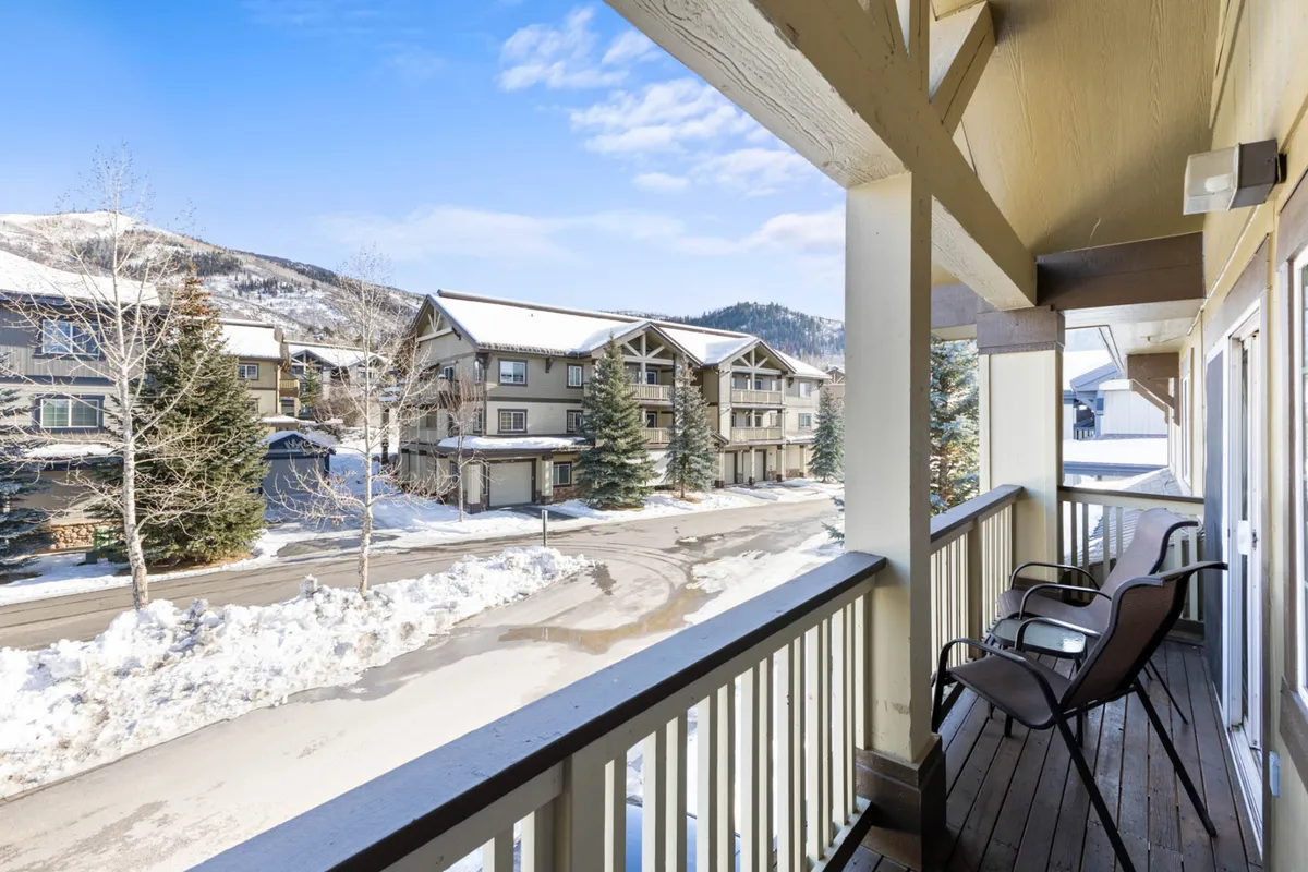 A serene balcony view overlooking a snow-covered ground and distant mountains, inviting guests to relax after a day on the slopes. The outdoor seating area provides a perfect spot to enjoy the fresh mountain air and scenic vistas.