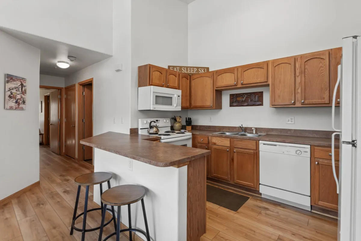 A warm kitchen scene features a central island, wooden cabinetry, and modern appliances, all bathed in soft, welcoming light. The setup encourages cooking, casual chats, and shared meals, reflecting a space where delicious memories are made.