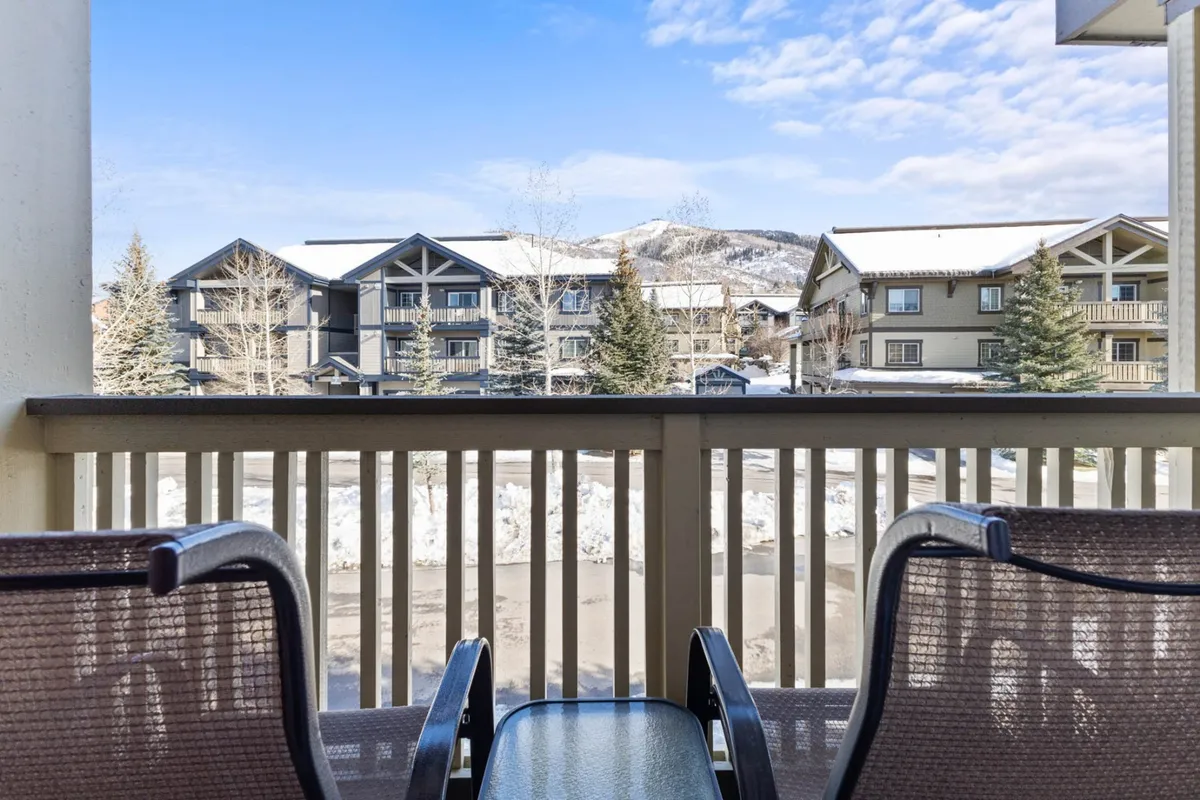 This exterior image features a private balcony with two chairs, offering expansive views of snow-covered mountains and the surrounding village buildings. The balcony setting is peaceful, inviting guests to relax, enjoy morning coffee, or soak in the mountain scenery right outside their accommodation.